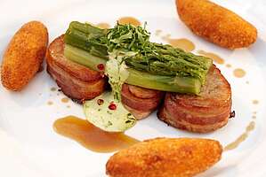 Fleischmedaillons mit Grünspargel und Kroketten auf weißem Teller.