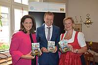 2 Frauen und ein Mann präsentieren lächelnd das Buch „Hier schmeckt's – 129 ausgezeichnete Gasthäuser in Bayern“.