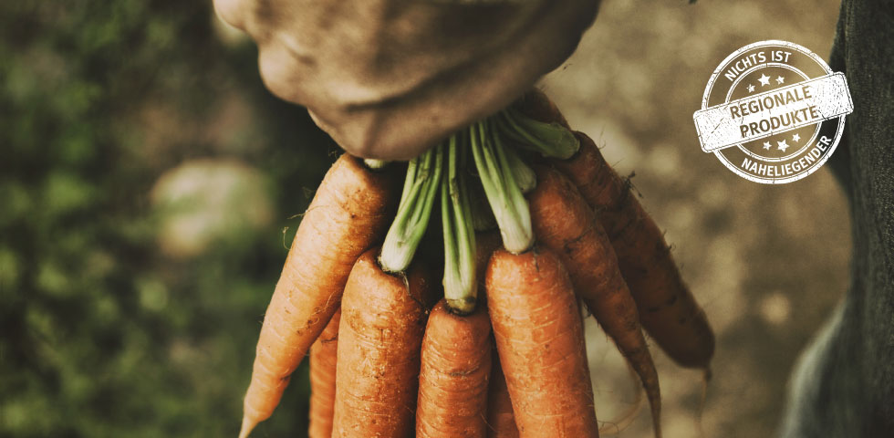 Hand hält Bündel Karotten am Möhrengrün, rechts oben weißes Siegel mit Aufschrift „Regionale Produkte – nichts ist naheliegender“